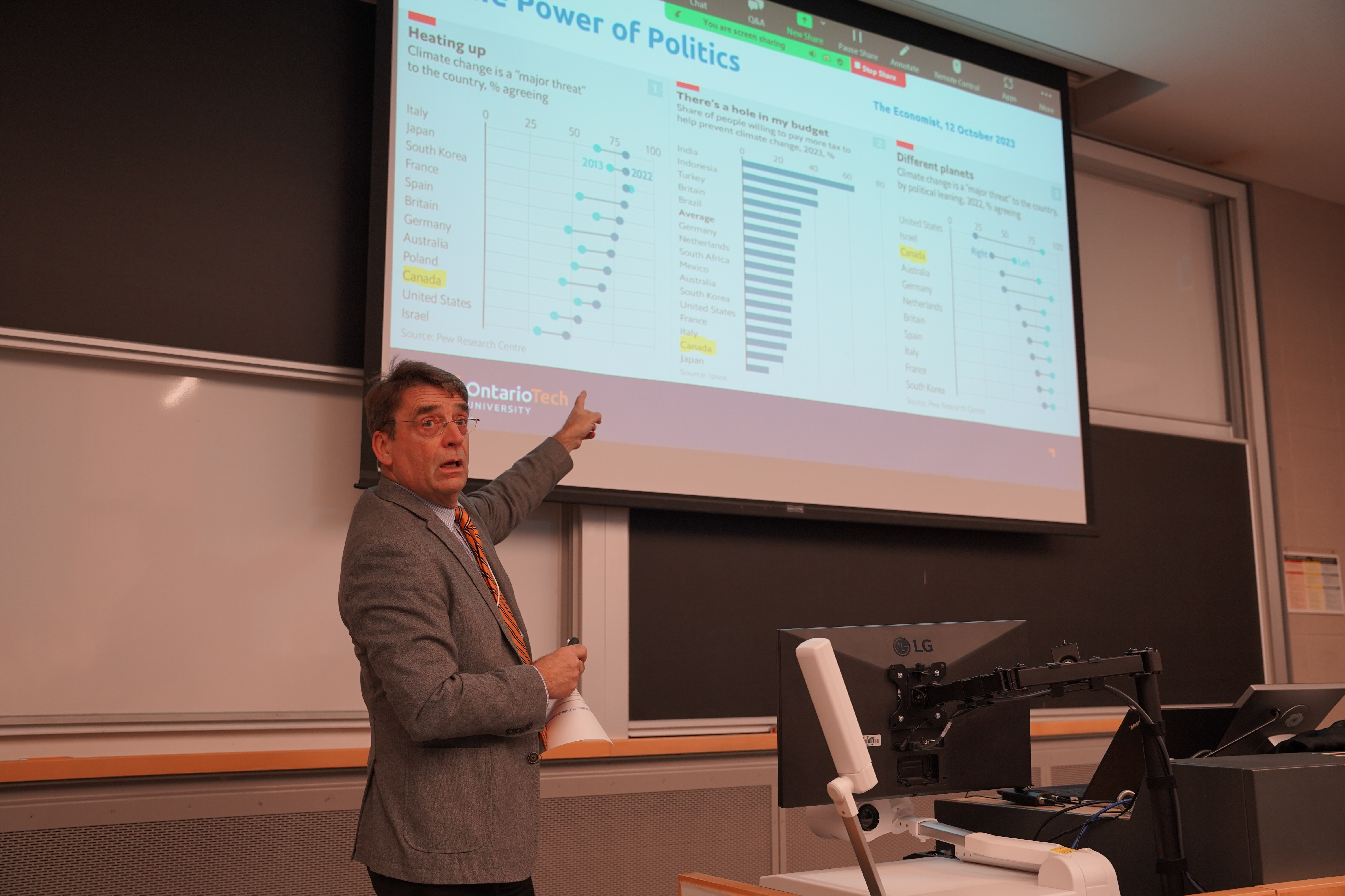 A man stands pointing at a presentation behind him that includes several graphics.